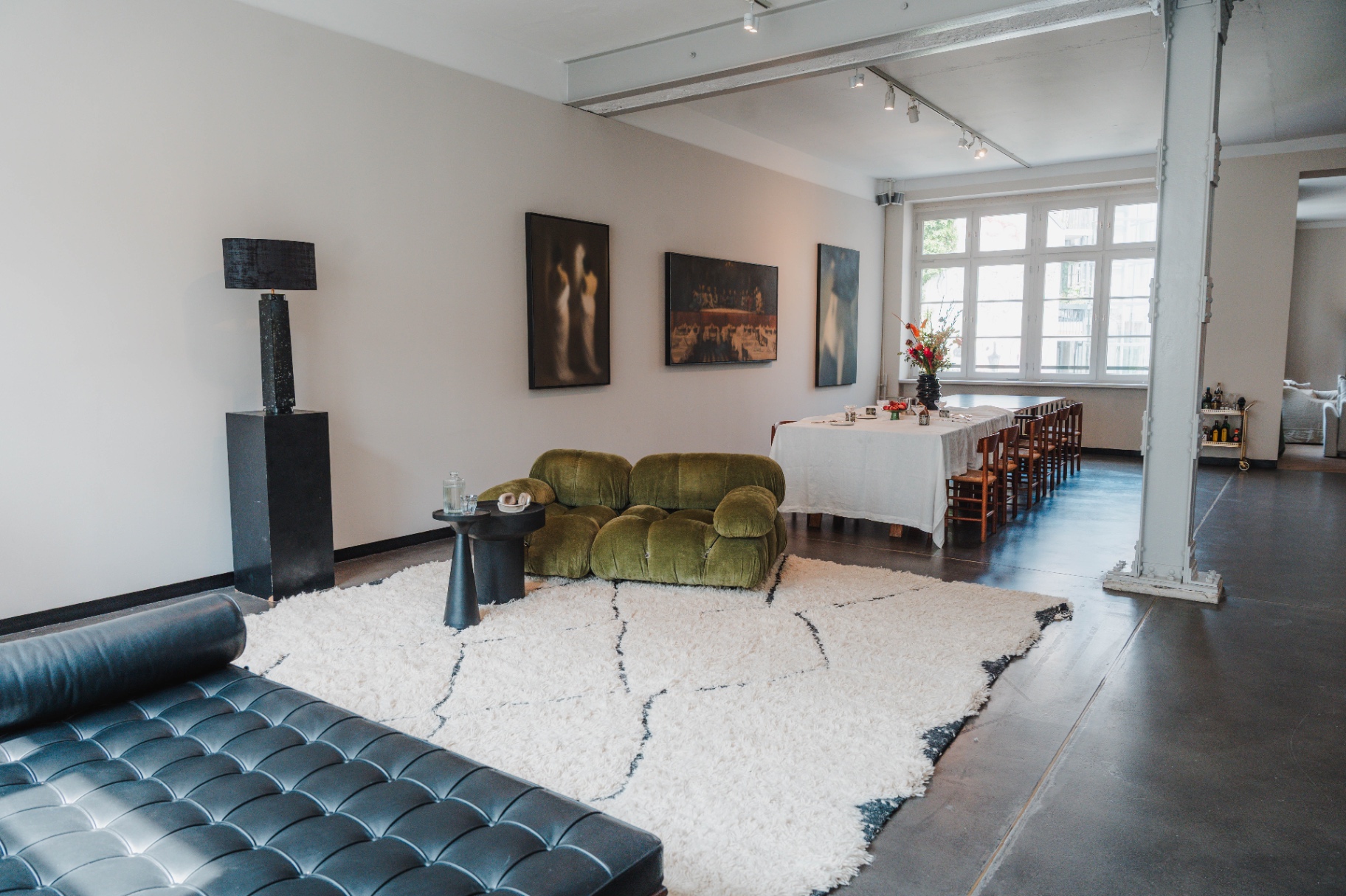 Loftansicht mit schwarzem Ledersofa, grüner Mario Bellini Camaleonda, Berber-Teppich und langem Esstisch